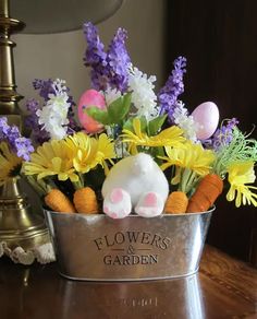 a metal bucket filled with flowers and stuffed animals sitting on top of a wooden table