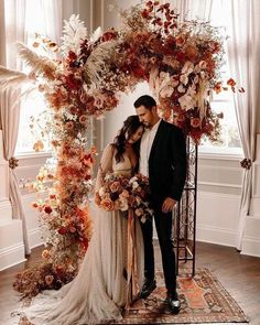 a man and woman are standing under an arch made out of flowers, leaves and branches