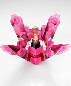 an origami wine bottle holder with pink flowers and roses on the bottom, holding a champagne bottle