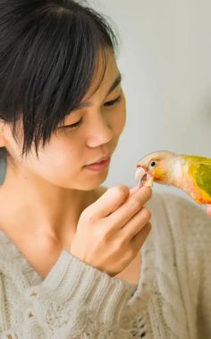 a woman holding a bird in her hand and looking at it's beaks