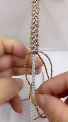 two hands are working on a piece of silver and gold chain