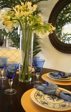 a dining room table set with blue and white plates, place settings and flowers in a vase