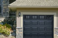 a black garage door is shown in front of a house with stone steps and landscaping