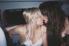 two young women are kissing in the back of a car with their backs to each other