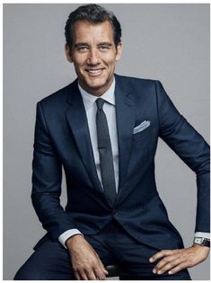 a man in a suit and tie is sitting on a stool smiling at the camera