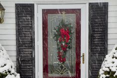 a red front door with wreaths on it and snow falling around the outside doors