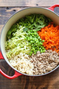 a pot filled with rice, carrots and other veggies on top of a wooden table