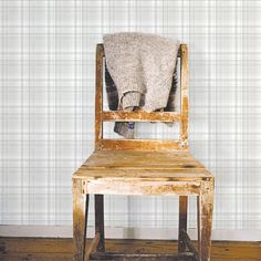 an old wooden chair with a blanket on it's back sitting in front of a wall