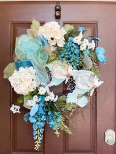 a wreath with blue and white flowers hanging on a brown front door, next to a red door