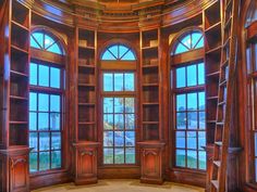 an empty room with large windows and wooden bookshelves