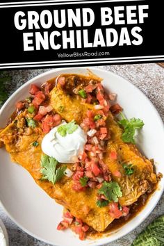 an enchilada on a white plate topped with sour cream and cilantro