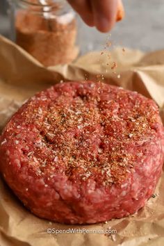 a person sprinkling seasoning on top of a raw hamburger pattie burger