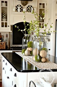 two vases filled with flowers on top of a black counter in a white kitchen