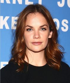 a woman with brown hair and blue eyes wearing a black top is looking at the camera