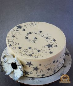 a white cake with stars on it sitting on top of a silver plate next to a flower