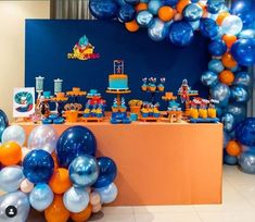 a birthday party with balloons and cake on the table in blue, orange and white colors