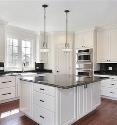 a large kitchen with white cabinets and black counter tops, an island in the middle