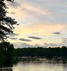 a lake surrounded by trees and boats under a cloudy sky