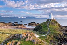 a white lighthouse sitting on top of a lush green hillside next to the ocean with mountains in the background