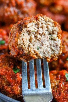 a close up of meatballs on a fork in a pan with sauce and parsley