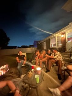 a group of people sitting around a fire pit on a patio at night with the sky in the background