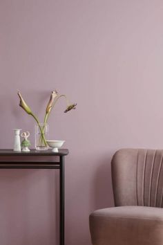 a chair and table with vases on it in front of a wall painted lilac