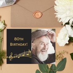 an old man's 80th birthday card with music notes and flowers next to it