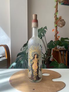 an empty bottle sitting on top of a wooden table next to a potted plant