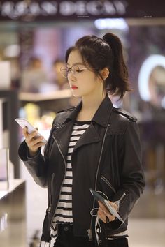 a woman in glasses is looking at her cell phone while standing on the airport terminal