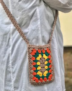 a woman wearing a white shirt is holding a crocheted bag with flowers on it