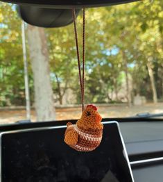 a small stuffed animal hanging from the dashboard of a car with trees in the background