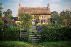 a house surrounded by flowers and greenery with a gate leading to the front door