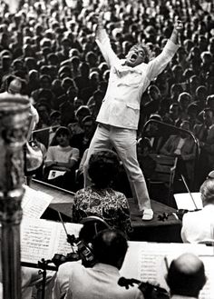 a man standing on top of a stage in front of an audience with his arms up