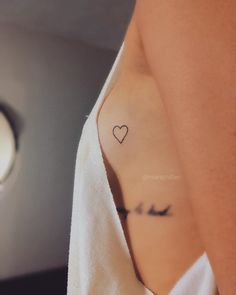 a woman with a small heart tattoo on her left side arm and chest, wrapped in a white towel