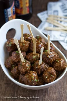 meatballs with toothpicks in a white bowl on a wooden table next to beer