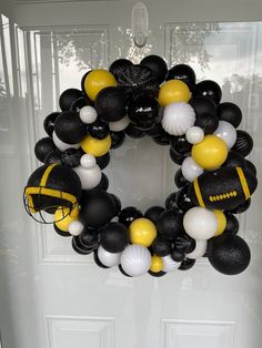 a football wreath with black, white and yellow balloons hanging on the front door to welcome you