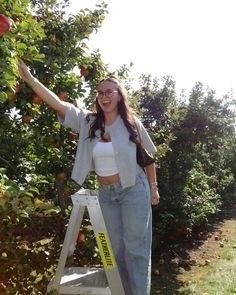 a woman is standing on a ladder in an apple orchard and smiling at the camera