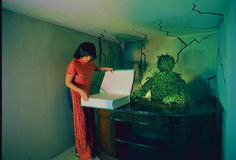 a woman standing in front of a box filled with green plants on top of a table