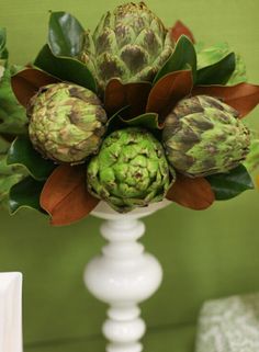 an artichoke arrangement in a white vase on a table with green wallpaper