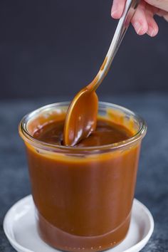 a spoon is being used to dip caramel sauce in a glass bowl on a plate