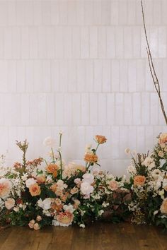 an arrangement of flowers in front of a white brick wall with wood flooring and wooden floors