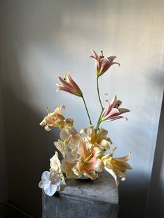 a vase filled with flowers sitting on top of a wooden block next to a wall