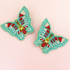 pair of blue and red beaded butterfly shaped brooches on pink surface with white background