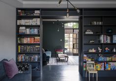 a living room filled with furniture and bookshelves next to a doorway that leads to a patio