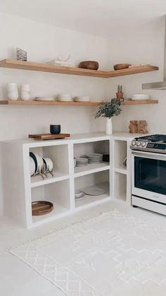 a white kitchen with open shelving and plates on the counter top, including an oven