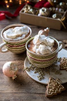 two cups of hot chocolate with whipped cream on top and christmas decorations around the edges