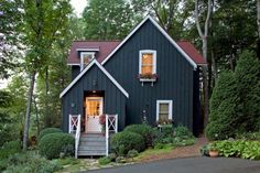 a black house with white trim and two windows on the front, surrounded by trees