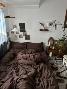 an unmade bed with brown sheets and pillows in a bedroom next to a window