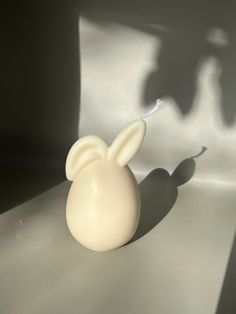 a white vase with an animal's shadow on the wall next to it and a toothbrush in its mouth