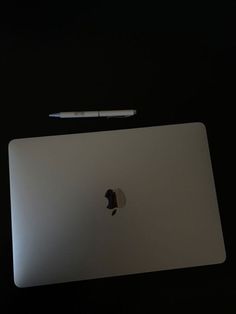 an apple laptop computer sitting on top of a black table next to a white pen